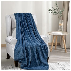 A soft blue textured blanket draped over a light gray armchair, next to a small round table with a glass vase holding branches.