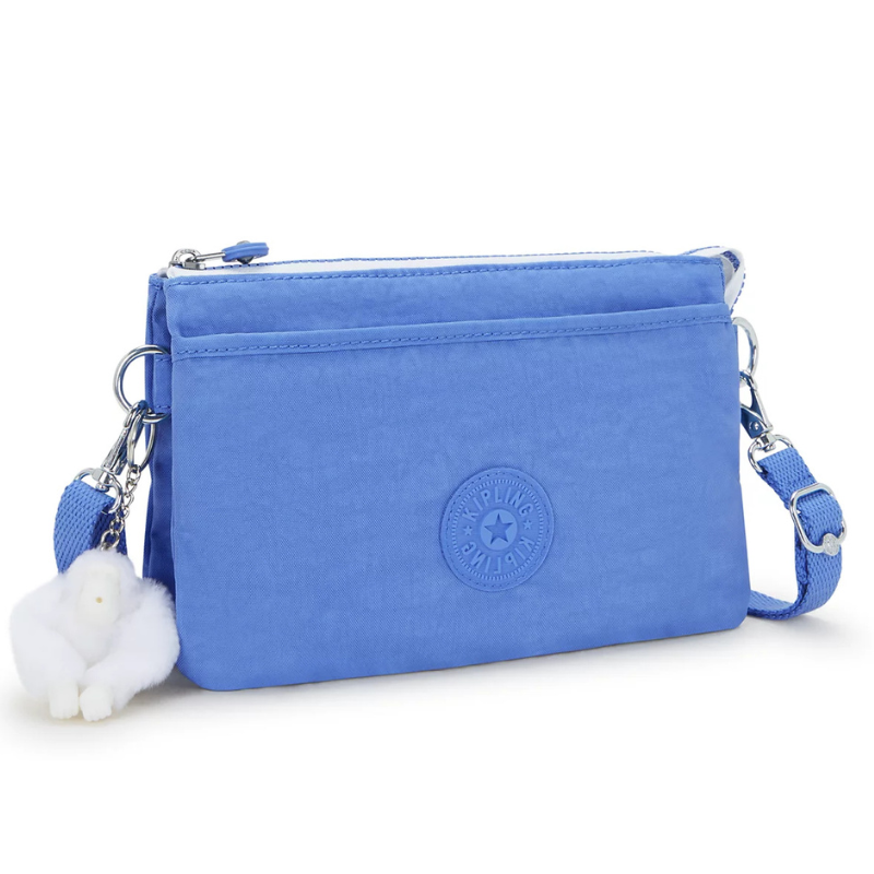 Blue crossbody bag with a detachable strap and a white fluffy keychain, featuring a circular logo on the front.