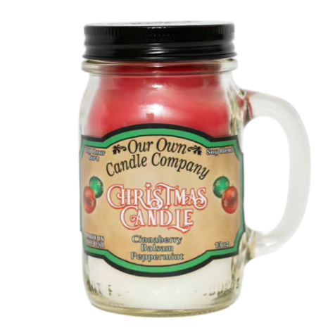 A jar candle labeled \“Our Own Candle Company Christmas Candle\“ with scents of cinnamon, balsam, and peppermint, housed in a glass mug with a handle.
