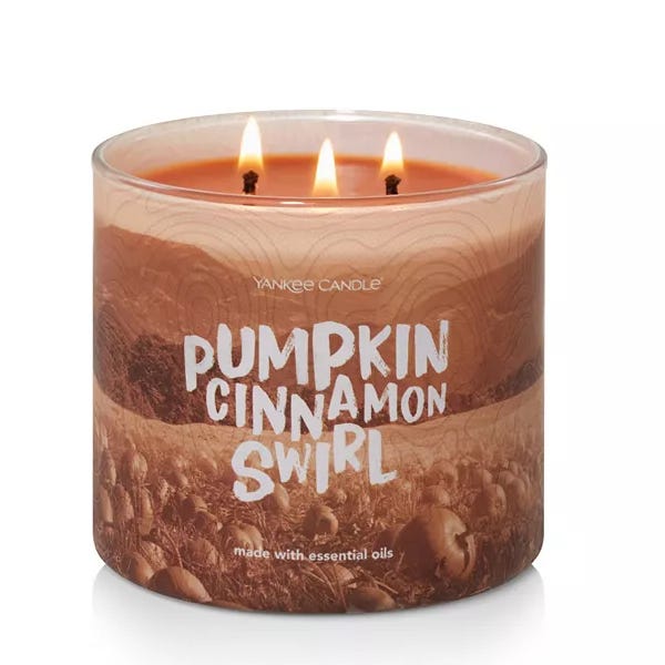 Yankee Candle Pumpkin Cinnamon Swirl is a 14.5oz candle with three wicks, featuring a warm, autumn-inspired scent of pumpkin and cinnamon. It is made with essential oils and has a decorative label showcasing a pumpkin field.