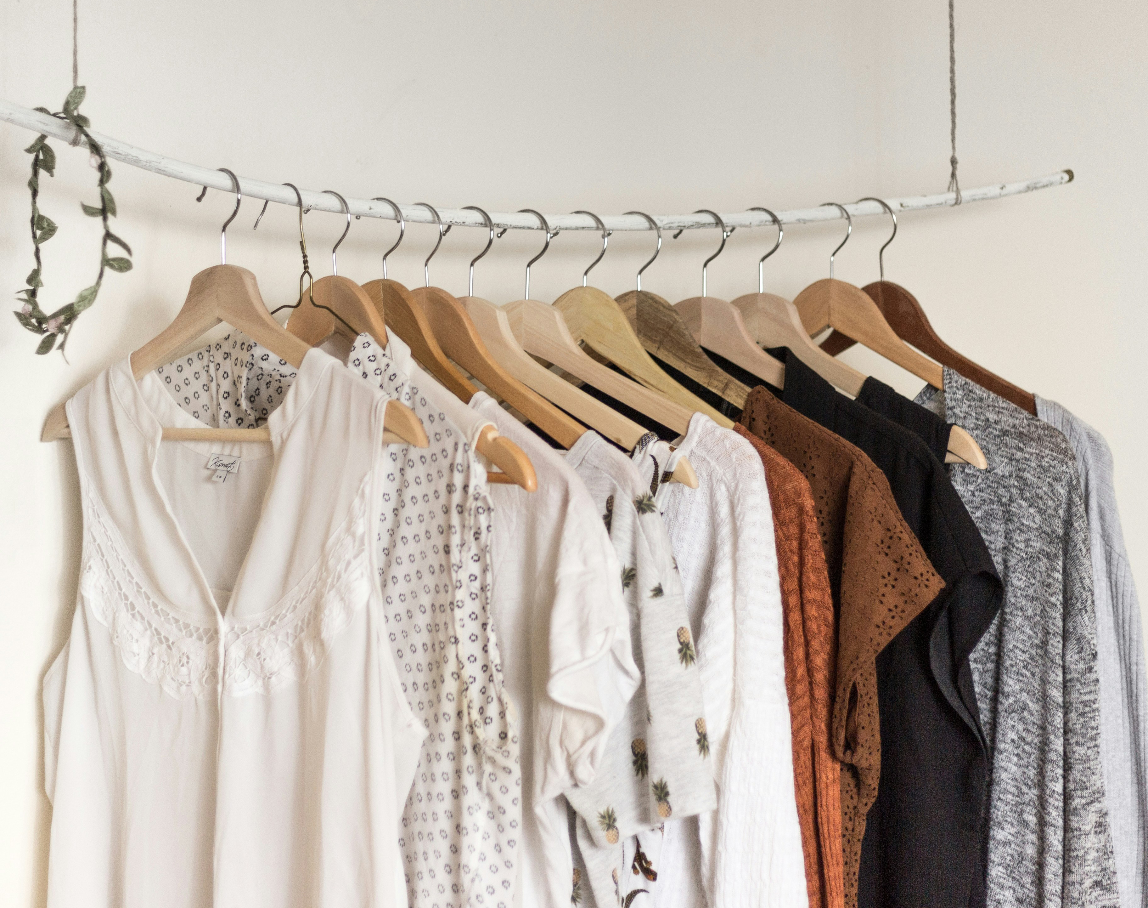 A variety of women's tops on wooden hangers, including white blouses with lace and patterned details, and darker casual shirts.