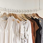 A variety of women's tops on wooden hangers, including white blouses with lace and patterned details, and darker casual shirts.