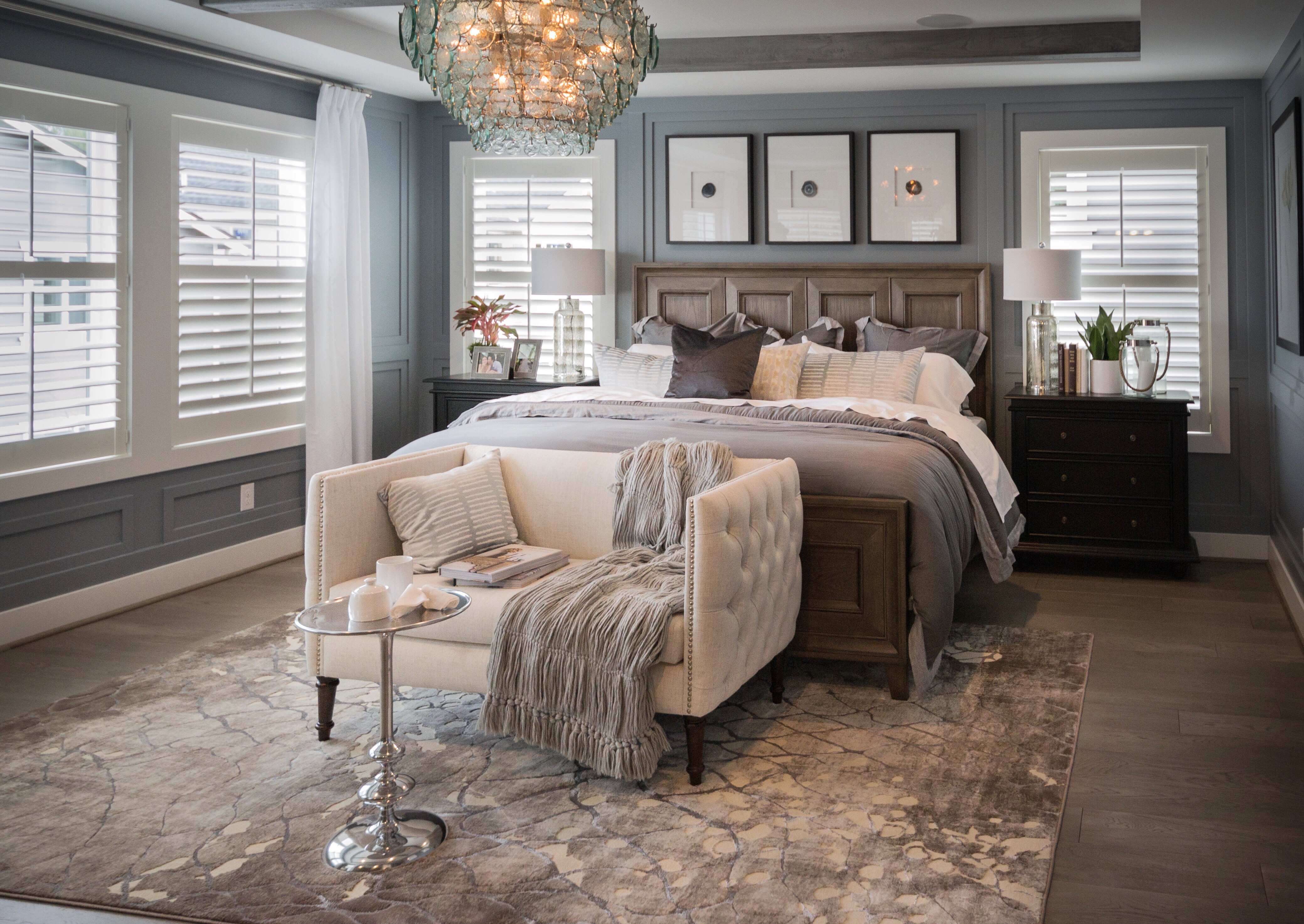 Elegant bedroom with a large bed, side tables, a sofa with a throw, and a chandelier.