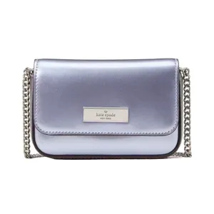 Metallic lavender crossbody bag with a chain strap and a rectangular metal logo plate on the front.