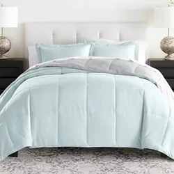 A light blue reversible comforter set features a stitched grid pattern, accompanied by matching pillow shams. It sits atop a bed with a cushioned white headboard, flanked by two black nightstands and lamps with textured bases.