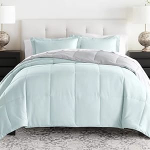 A light blue reversible comforter set features a stitched grid pattern, accompanied by matching pillow shams. It sits atop a bed with a cushioned white headboard, flanked by two black nightstands and lamps with textured bases.