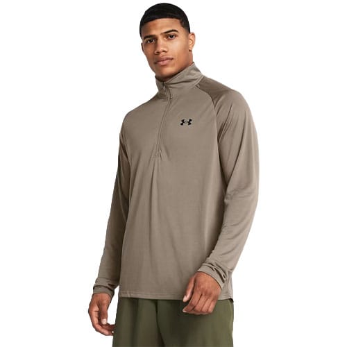 A man wearing an Under Armour long-sleeve, quarter-zip athletic top in a neutral color, paired with green pants.