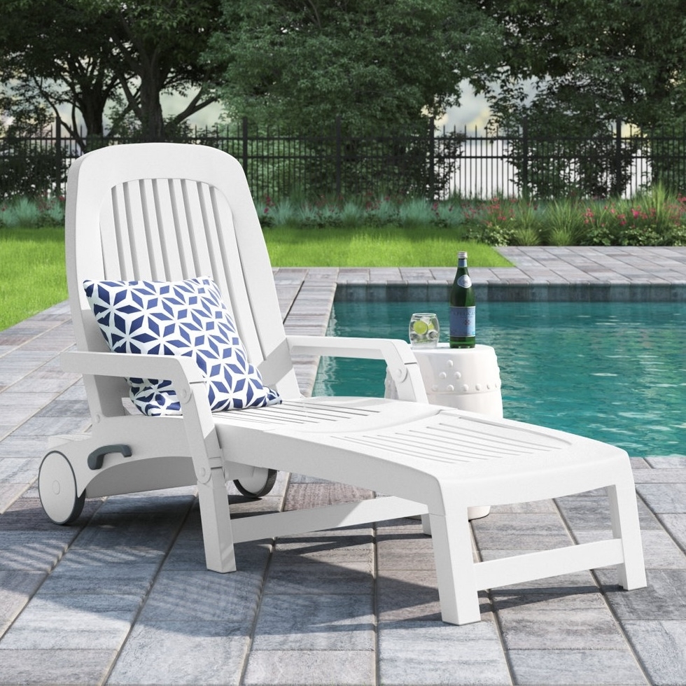 White poolside chaise lounge with adjustable backrest, geometric blue and white cushion, and a small round side table holding a bottle and a drink.