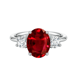 A ring featuring an oval red gemstone at the center flanked by two smaller round diamonds, set in a silver band.