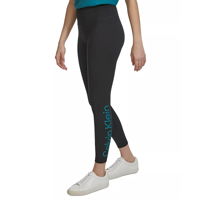 High-rise 7/8 leggings in a dark shade, featuring the Calvin Klein logo on the lower left leg and paired with white sneakers.