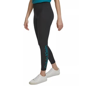 High-rise 7/8 leggings in a dark shade, featuring the Calvin Klein logo on the lower left leg and paired with white sneakers.