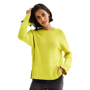 A woman wears a bright yellow sweater with ribbed detailing at the cuffs and hem, paired with dark pants, while adjusting her hair.