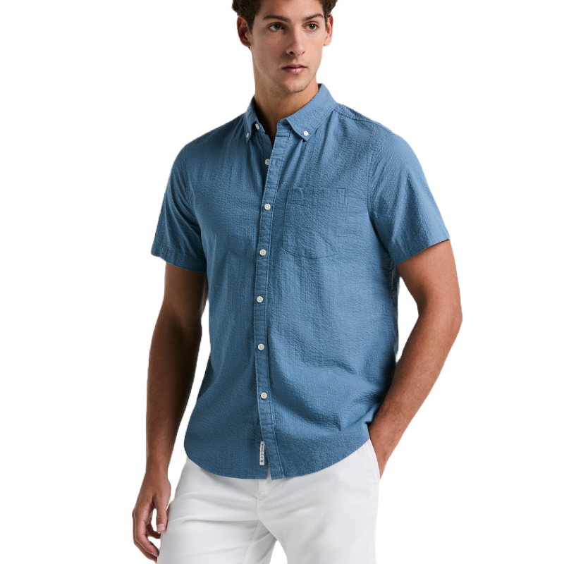 Blue short-sleeve seersucker shirt, button-down with a front pocket and a textured fabric. Paired with white pants.