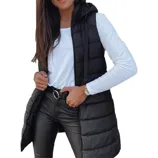 A woman is wearing a black puffer vest over a white long-sleeve shirt, black leather pants, and a belt. She has a watch on her left wrist.