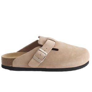 Beige suede clogs with a buckle strap, featuring a closed toe and open heel, designed for comfort with a water-repellent finish and a black sole.