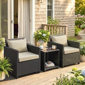 Outdoor patio set featuring two wicker armchairs with beige cushions and a small matching side table, adorned with potted plants and a mug on the table.