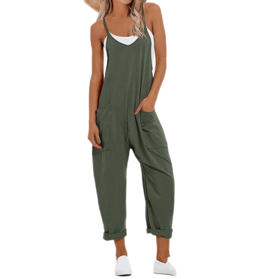 A woman wearing an olive green, loose-fitting jumpsuit with spaghetti straps and side pockets, paired with white sneakers.
