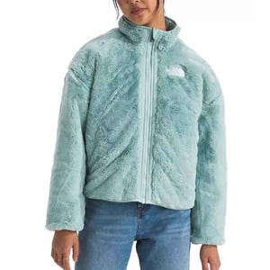 Light blue, plush, reversible full-zip jacket with a stand collar and the logo on the chest, paired with blue jeans.