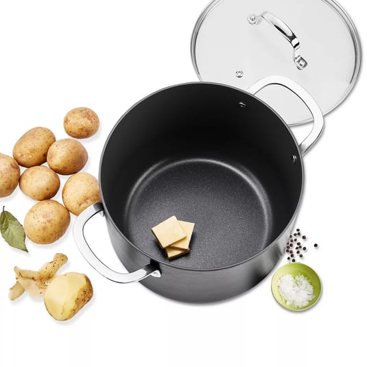 A nonstick pot with a lid is shown alongside potatoes, a bay leaf, peeled potato pieces, butter squares, salt in a green bowl, and peppercorns.