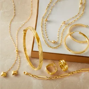 A collection of gold jewelry including necklaces, hoop earrings, a bangle, stud earrings with heart-shaped charms, and a link bracelet arranged on a flat surface.