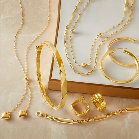 A collection of gold jewelry including necklaces, hoop earrings, a bangle, stud earrings with heart-shaped charms, and a link bracelet arranged on a flat surface.