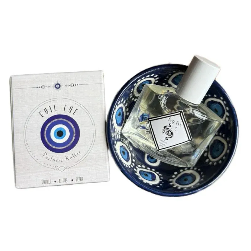 Evil Eye Perfume Roller set featuring a bottle of perfume placed in a decorative bowl with blue eye patterns, accompanied by packaging labeled with notes of vanilla, citrus, and cedar.