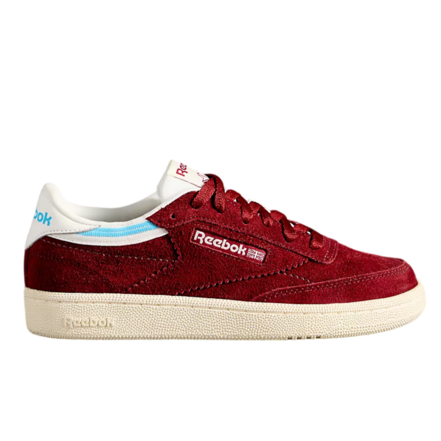 A Reebok sneaker in dark red suede with white and blue accents, featuring Reebok branding on the side and tongue, paired with a textured white sole.