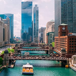 A scenic view of the Chicago River with bridges and boats, flanked by high-rise buildings and a historic clock tower.