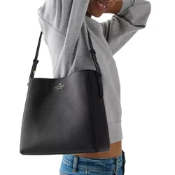 A person carries a black Kate Spade New York tote bag with adjustable straps, wearing a gray sweatshirt and blue jeans.