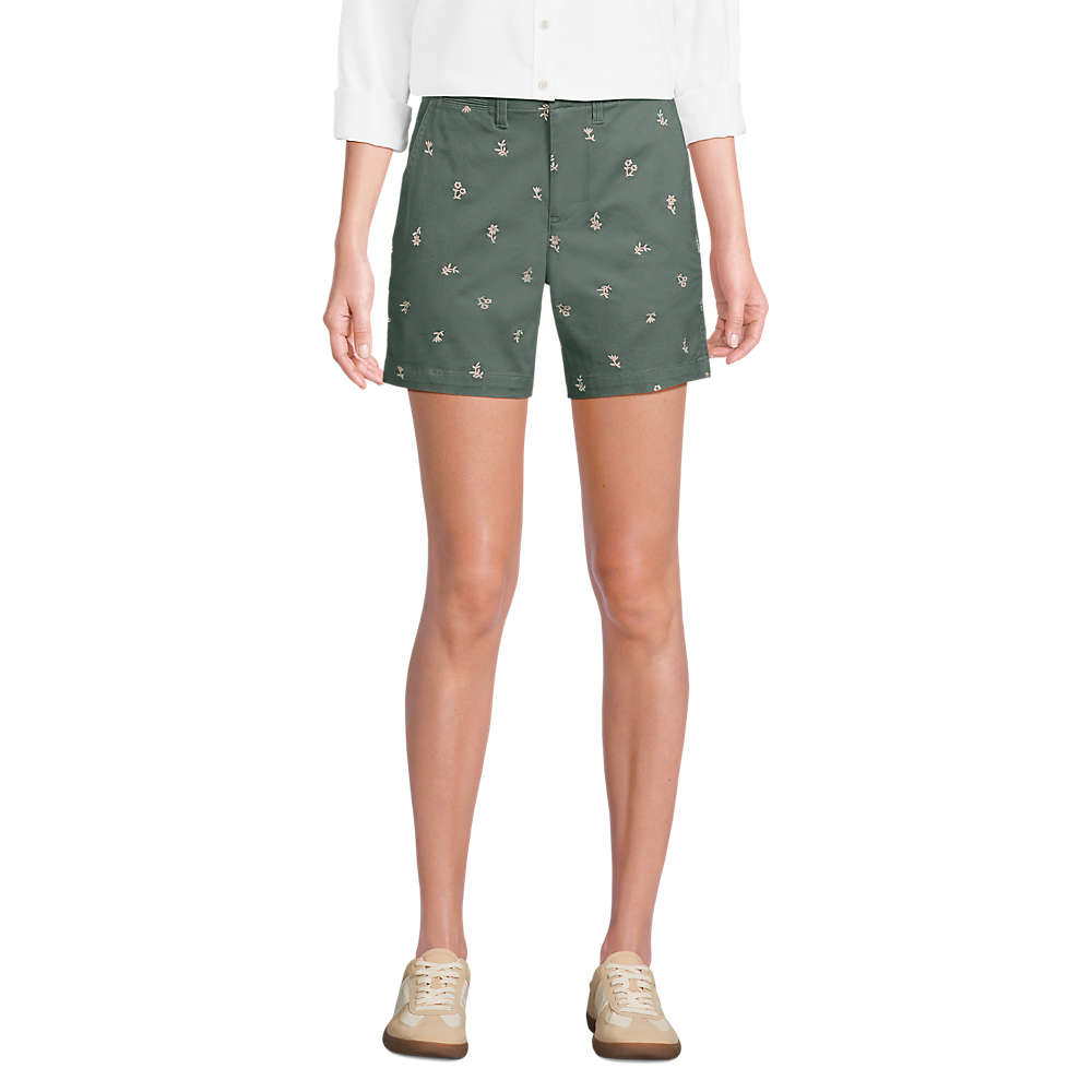 Green shorts with small floral embroidery paired with a white long-sleeve shirt and beige sneakers.