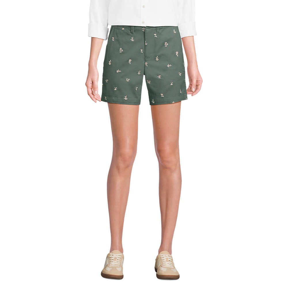 Green shorts with small floral embroidery paired with a white long-sleeve shirt and beige sneakers.