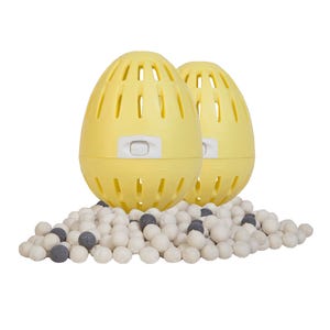 Two yellow egg-shaped laundry items with slotted designs are surrounded by small white and gray spheres.