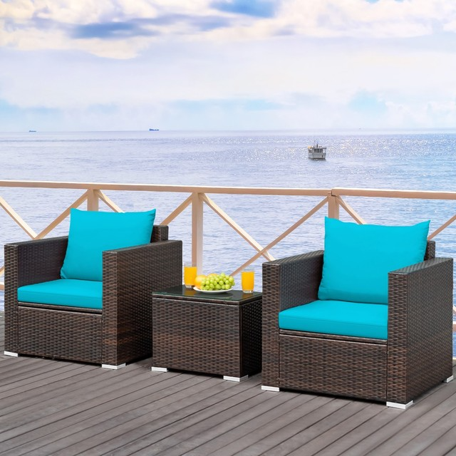 Outdoor rattan furniture set with turquoise cushions on a wooden deck by the sea.