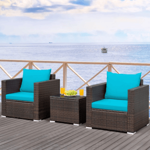 Outdoor rattan furniture set with turquoise cushions on a wooden deck by the sea.