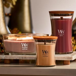 Three WoodWick candles are displayed: a rectangular one labeled \“PATCHOULI CHÈRE,\“ a reddish-brown one labeled \“ROUGE OUD,\“ and a beige one labeled \“GOLDEN BOURBON.\“