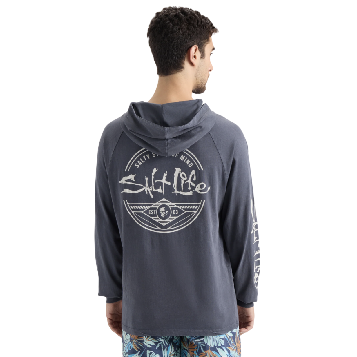 A man wearing a hooded long-sleeve shirt with \“Salt Life\“ printed on the back and sleeve, paired with tropical-patterned shorts.