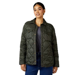 A woman is wearing an olive green quilted jacket with button closures, two chest pockets, and a shirt collar. She pairs it with a gray top and blue jeans.