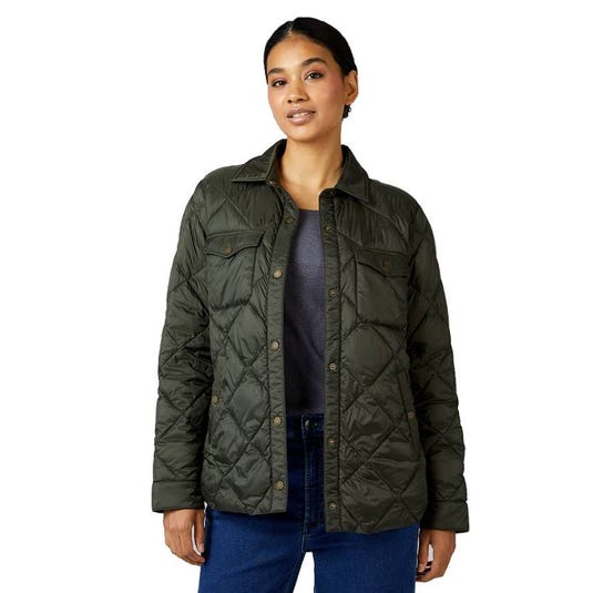 A woman is wearing an olive green quilted jacket with button closures, two chest pockets, and a shirt collar. She pairs it with a gray top and blue jeans.