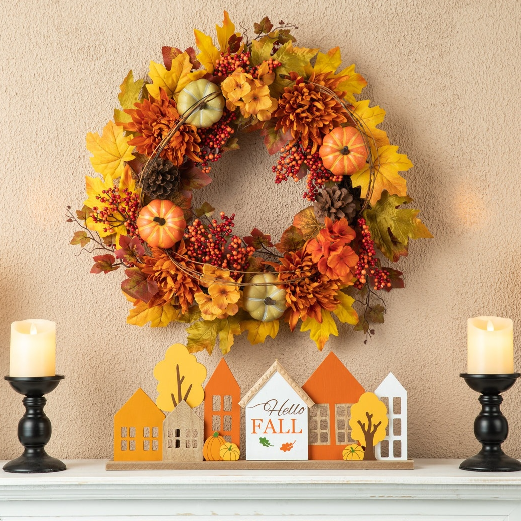 Autumn-themed wreath with pumpkins, flowers, and berries, and a decorative \“Hello Fall\“ sign set on a mantel, flanked by black candle holders with lit candles.