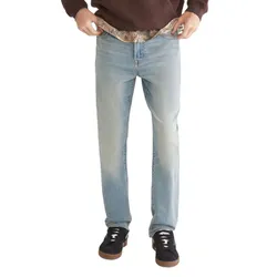 A person wearing light blue jeans and black sneakers with white laces, paired with a brown hoodie. The jeans are being held at the waistband, revealing camouflage-patterned fabric underneath.