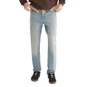 A person wearing light blue jeans and black sneakers with white laces, paired with a brown hoodie. The jeans are being held at the waistband, revealing camouflage-patterned fabric underneath.