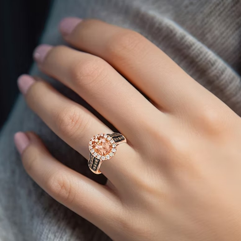 A hand with painted nails is wearing a rose gold ring featuring a large pink gemstone surrounded by smaller clear diamonds.