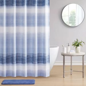 Blue and white striped shower curtain, circular mirror, white bathtub, side table with bathroom accessories, and a blue bathmat.