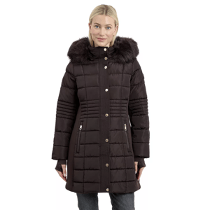 A woman wears a dark brown hooded puffer coat with a faux fur trim and gold-tone button details, paired with dark jeans.