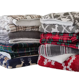 A stack of folded blankets featuring various patterns, including plaid and holiday-themed designs with reindeer and snowflakes, in colors such as red, gray, blue, and green.