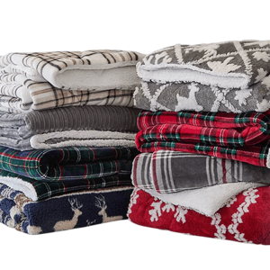 A stack of folded blankets featuring various patterns, including plaid and holiday-themed designs with reindeer and snowflakes, in colors such as red, gray, blue, and green.