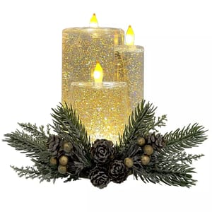 A set of three LED candles with glittery, illuminated surfaces, paired with a decorative base featuring pine branches, pinecones, and gold berries.