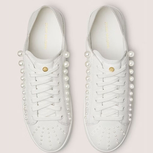 A pair of white sneakers with pearl embellishments on the sides and toes.