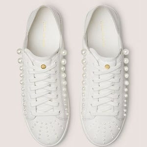 A pair of white sneakers with pearl embellishments on the sides and toes.