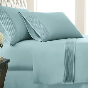 A pale blue bedding set featuring pillowcases and a flat sheet with pleated detailing displayed on a bed.